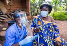 Ebola Horror: Camps in Congo LACK BASICS! Healthcare worker in PPE talks with elderly woman using a crutch outdoors