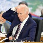 A political leader in formal attire appears deep in thought during a meeting