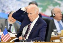 A political leader in formal attire appears deep in thought during a meeting