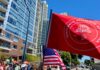Protesters march in a city street holding a large red flag and U.S. flags