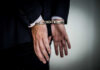 A person in a suit with hands cuffed behind their back