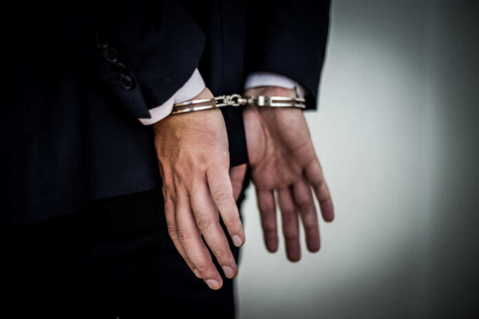 A person in a suit with hands cuffed behind their back