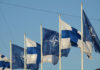 NATO’s Quiet Nuke Gambit Near Russia Flags of Finland and NATO waving in the wind against a clear blue sky