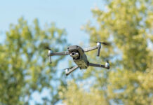 A drone flying against a backdrop of green trees and a blue sky