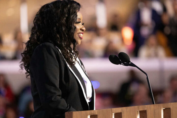 A woman in formal attire speaking at a podium with microphones