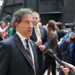 A public figure being interviewed amidst a crowd of reporters and onlookers