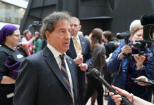 A public figure being interviewed amidst a crowd of reporters and onlookers