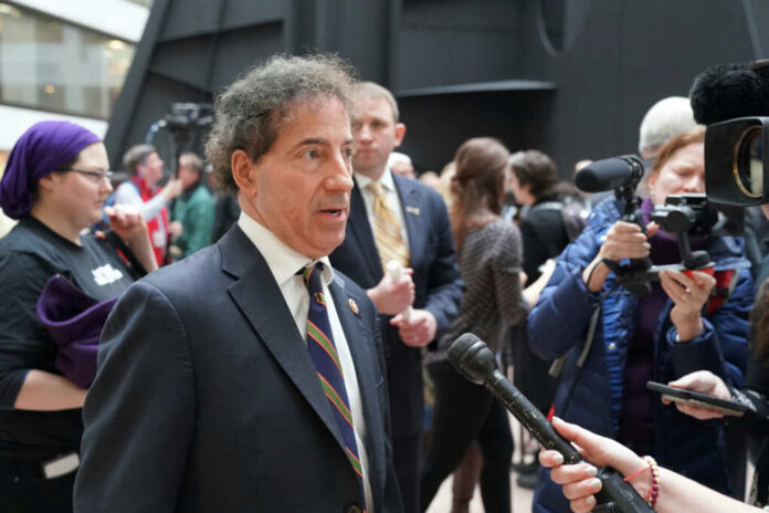 A public figure being interviewed amidst a crowd of reporters and onlookers