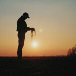 Silhouette of a farmer holding soil against a sunset backdrop