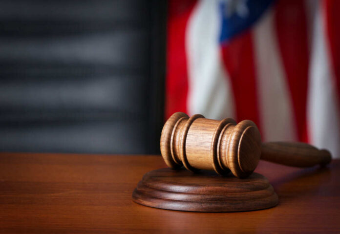 shutterstock_159118949 A wooden gavel resting on a round base with a blurred American flag in the background