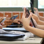 UK’s Big Brother Move Sparks Uproar Students in a classroom using smartphones for a group activity