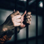 Parole Math Fails — Deadly Bill Comes Due Hands gripping prison bars in a dimly lit environment