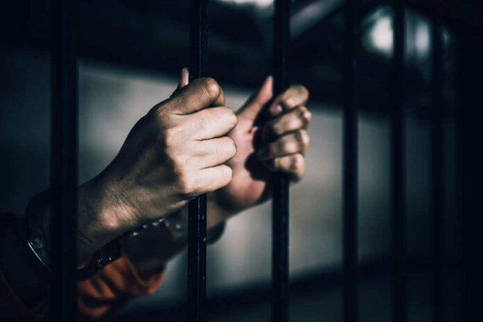 Hands gripping prison bars in a dimly lit environment