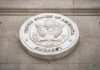 Diplomat Dead Abroad—Police Suspect Worse Seal of the United States Embassy displayed on a wall