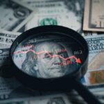 Magnifying glass over US dollar bills with stock market data displayed
