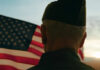 Decades Later, Gulf War Veterans Still Await Justice A veteran in uniform standing in front of an American flag during sunset