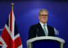 A political leader standing at a podium with a British flag in the background