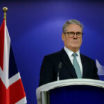 Shock Resignation — What Crushed The PM? A political leader standing at a podium with a British flag in the background