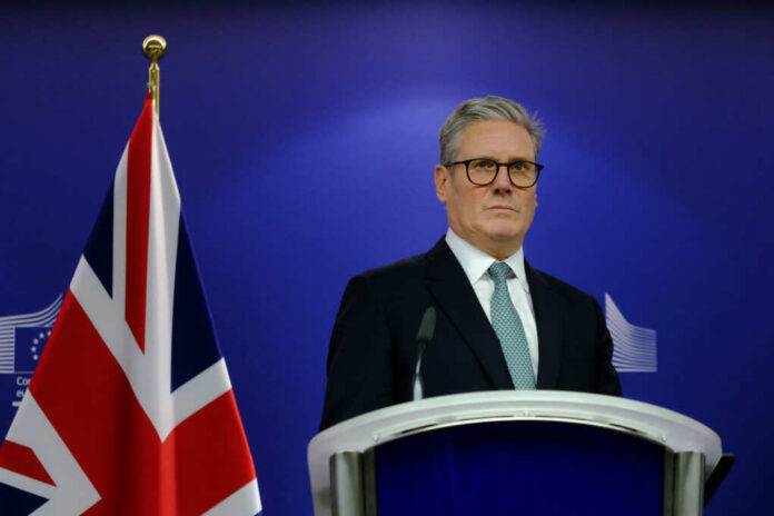A political leader standing at a podium with a British flag in the background