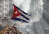 Power Crisis Triggers Daring Cuba Overhaul Tattered Cuban flag waving over a pile of rubble in a devastated urban landscape