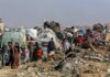 Displaced families with belongings crowd a rubble-strewn road