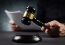 Track Meet Murder Splits America A gavel held above a sounding block with a person reading documents in the background