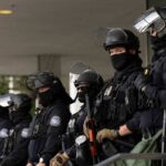 Police officers in riot gear stand in a line