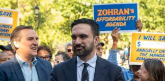 A politician speaking at a rally with supporters holding signs