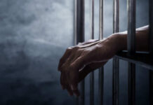 A close-up of hands gripping prison bars in a dimly lit environment