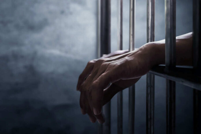 A close-up of hands gripping prison bars in a dimly lit environment