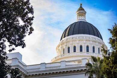 Capitol building dome framed by trees against a blue sky