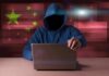 China Scoops 220M Voter Files Hooded figure using a laptop with red cybersecurity graphics