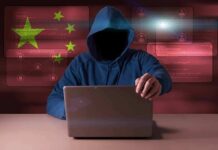Hooded figure using a laptop with red cybersecurity graphics