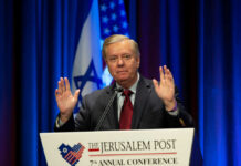 A speaker gesturing during a political conference with flags in the background