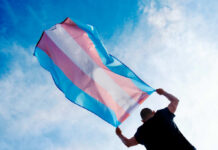 Emergency Call Over Seattle Resource Strain Person holding a transgender pride flag against a blue sky