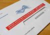 Mail-in ballot envelope with red label on wooden table
