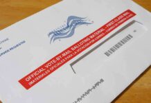 USPS Mail Ballot Rule Advances Mail-in ballot envelope with red label on wooden table