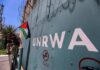 Man holding a Palestinian flag near a wall marked UNRWA