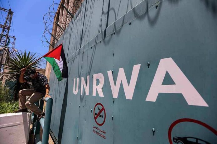 shutterstock_2320247939 Man holding a Palestinian flag near a wall marked UNRWA