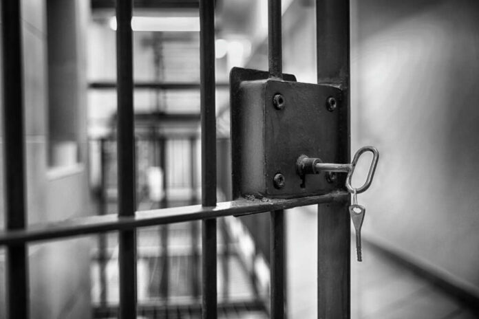 shutterstock_2402273361-1 Close-up of a jail cell lock with a key hanging