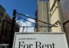 Housing Costs Meet Immigration Reality Sign indicating apartments available for rent against a blue sky