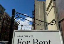 Housing Costs Meet Immigration Reality Sign indicating apartments available for rent against a blue sky