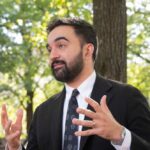 Man in a suit gesturing while speaking outdoors