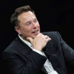Billionaire War Chest Reloads GOP Man in suit smiling, resting chin on hand.