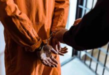 Casting Calls Allegedly Lured Teenage Victims Prisoner in orange jumpsuit handcuffed by officer