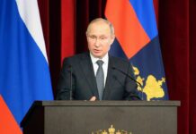 man in suit speaking at a podium with flags behind him