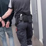 Security officer escorts handcuffed person down hallway