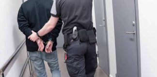 Security officer escorts handcuffed person down hallway