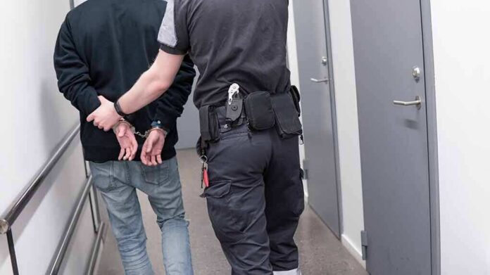 shutterstock_1082126789 Security officer escorts handcuffed person down hallway
