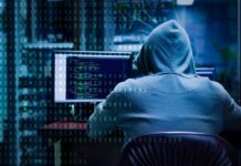 Ransomware Gangs Get U.S. Payback Person in hoodie working at computer with code on screens